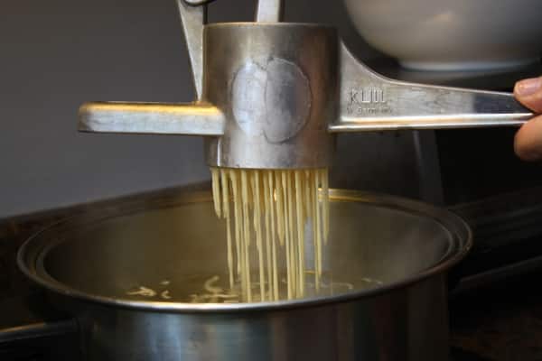 spaetzles getting pressed into a pot of boiling water