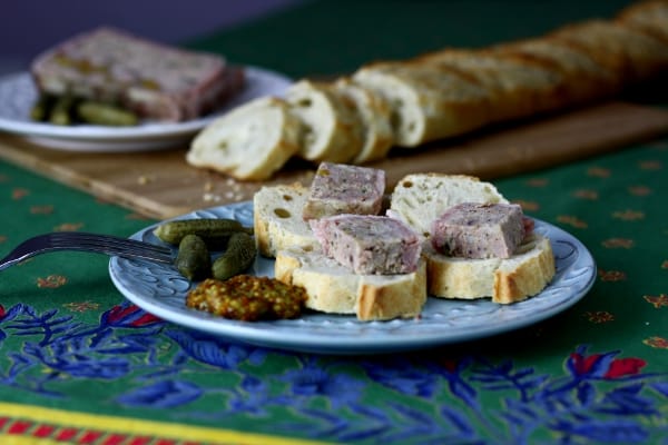terrine pieces with baguette on a plate with mustard and mini pickles 