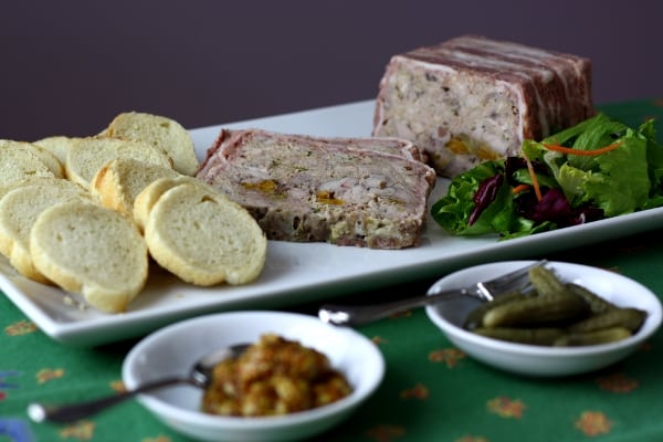 terrine de campagne on a plate with baguette slices and bowls of mustard and cornichons in the front