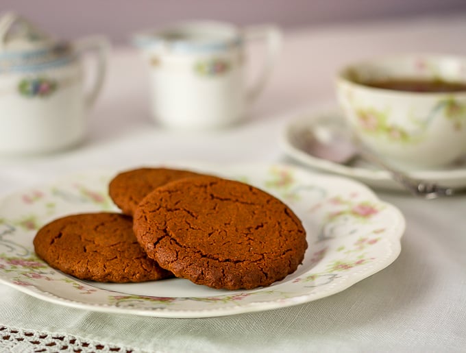 old fashioned cinnamon cookies on an antique plate with a cup of tea in the background