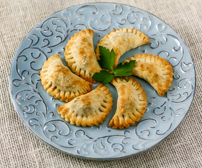 empanadas on a blue plate with a piece of cilantro in the middle 