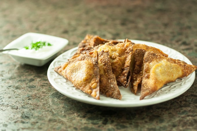 a white plate of fried samosas with sauce on the left
