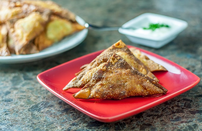 fried samosas on a plate with a serving dish in the back