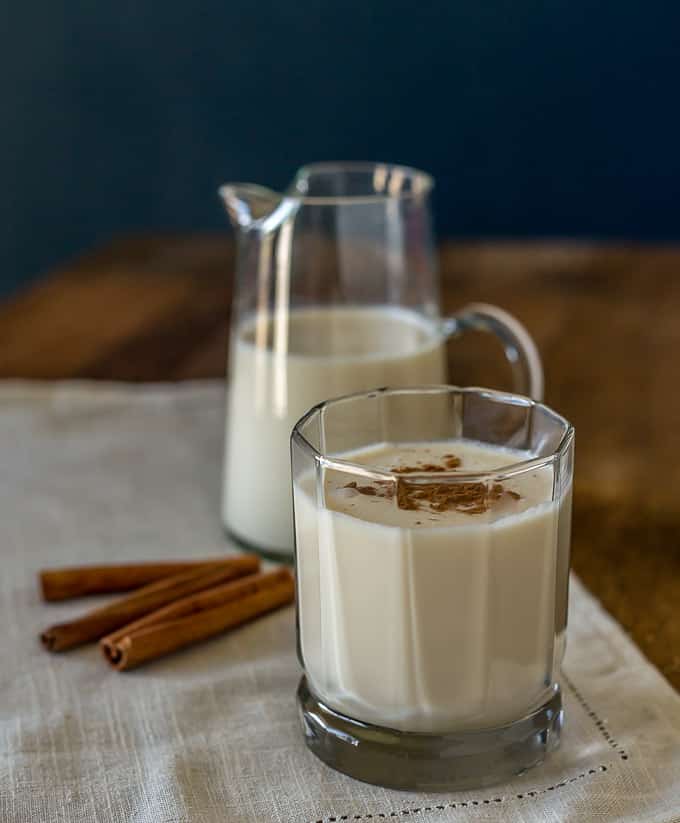 a closeup of coquito with cinnamon with cinnamon sticks and pitchers in the back