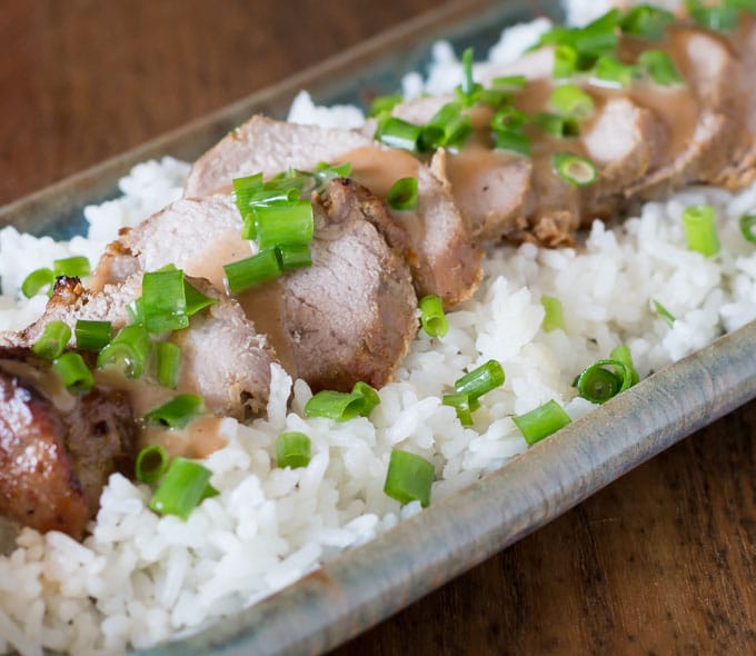 a closeup of thai pork loin on white rice with scallion pieces