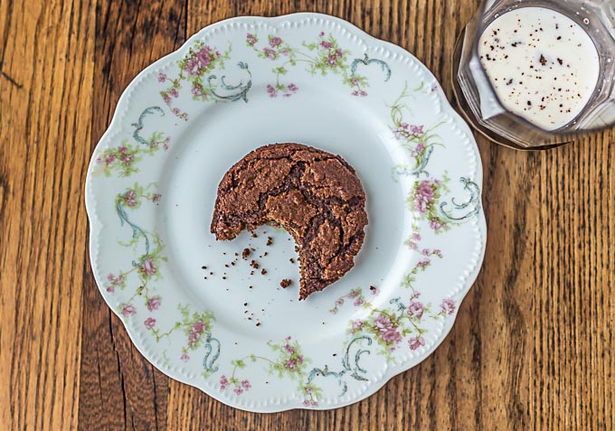an antique plate with a bitten chocolate cookie and a cup of milk