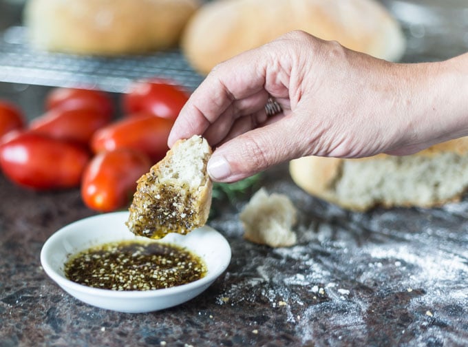a bowl of zatar and olive oil with bread dipping in and tomatoes in the back