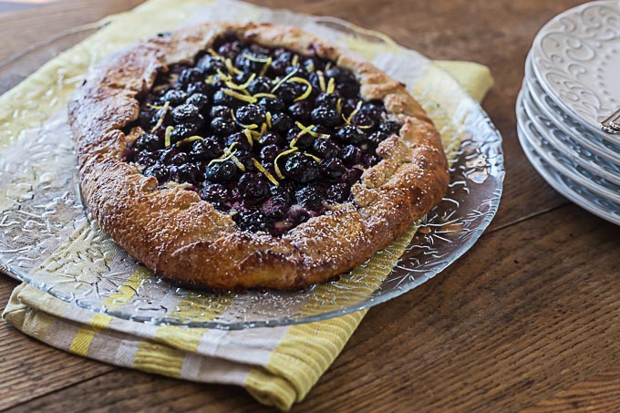 fresh baked blueberry crostata on a glass plate with a striped towel underneath