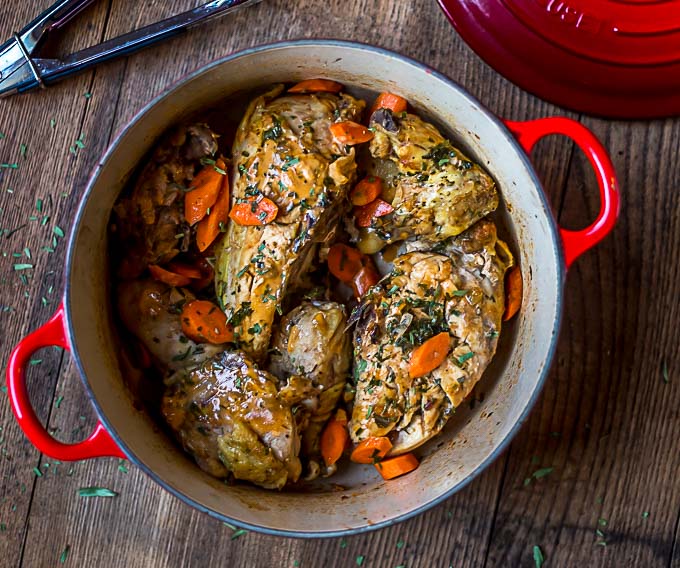 a closeup of a red dutch oven with tongs and tarragon chicken