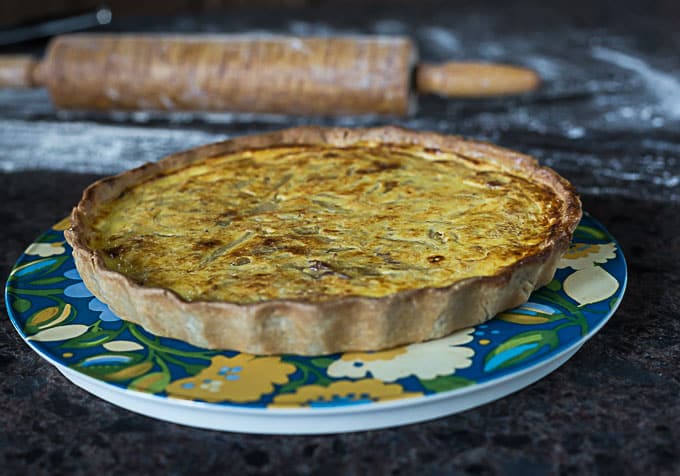 a fresh baked sweet onion quiche on a colorful plate with a rolling pin in the back
