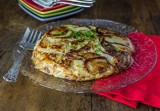 An italian potato pancake with onions on a plate with a fork and a red napkin underneath