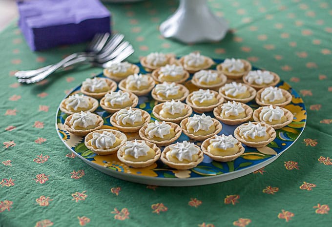 a colorful plate of mini lemon tarts with whip cream on a green tablecloth 