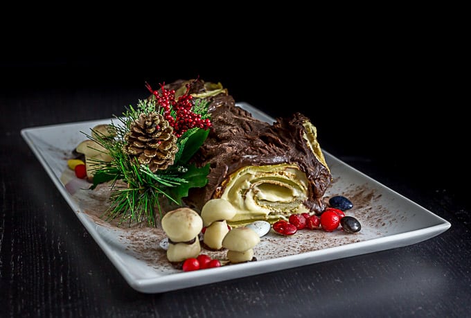 a French buche noel on a plate with marzipan berries, mushrooms, and some tree garnish