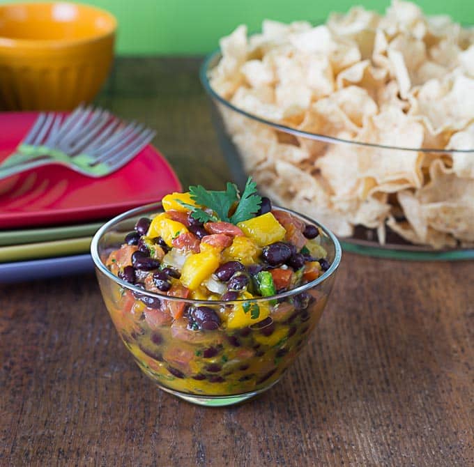 a closeup shot of mango black bean salsa with a bowl of chips in the background