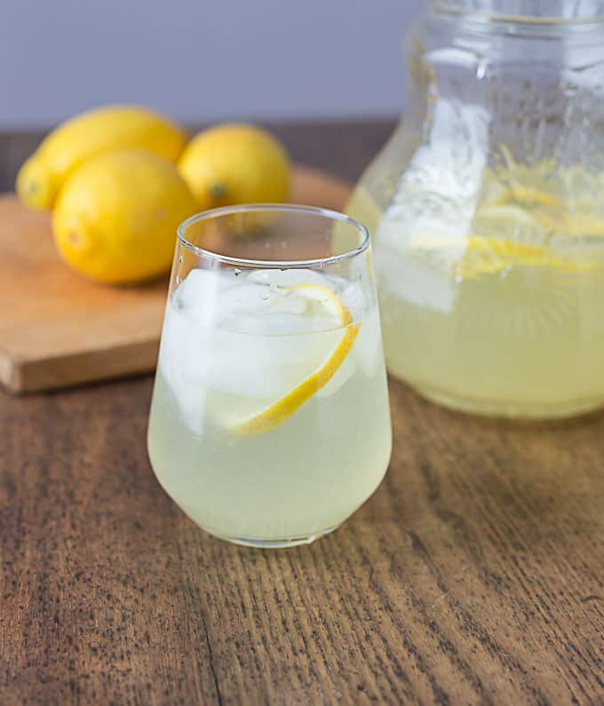 a closeup of a glass of rosewater lemonade with a pitcher and lemons in back