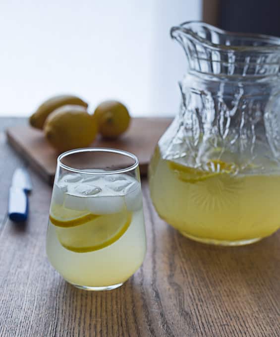 Rosewater lemonade in a glass pitches and served in a glass with lemons in the back