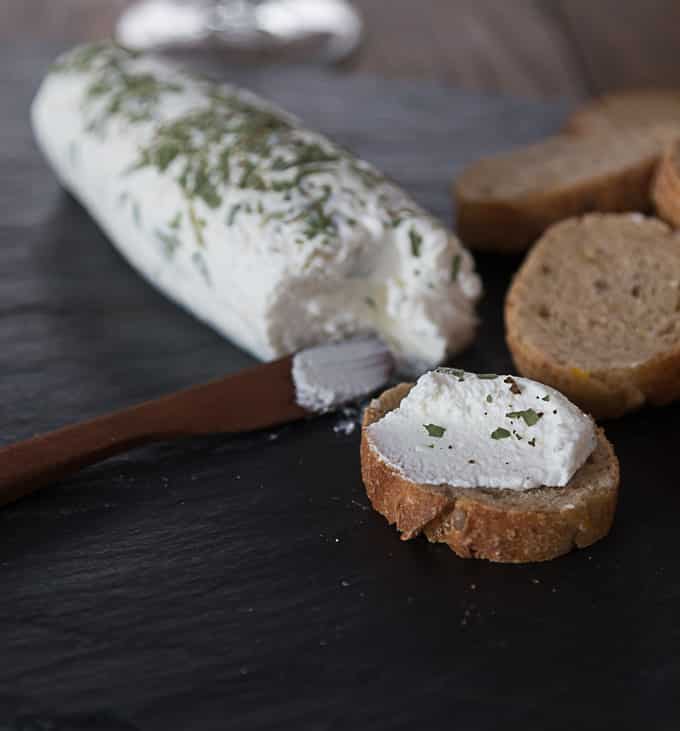 a roll of goat cheese with herbs and slices of brown bread spread with goat cheese