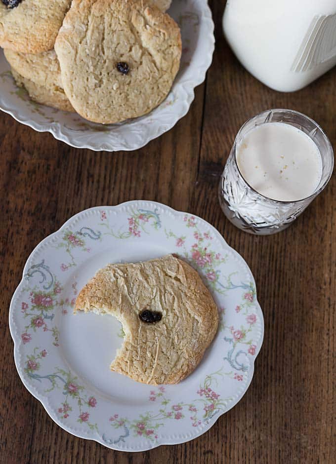 a bitten sugar cookie on a plate with a raisin in the middle and a glass of milk on the right