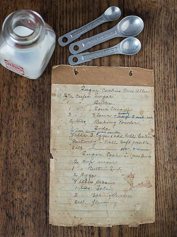 a page of an old recipe book with metal spoons and a glass cream container above 