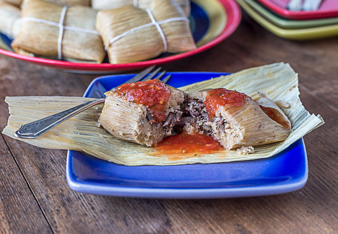 A tamale on a blue plate with red salsa. 