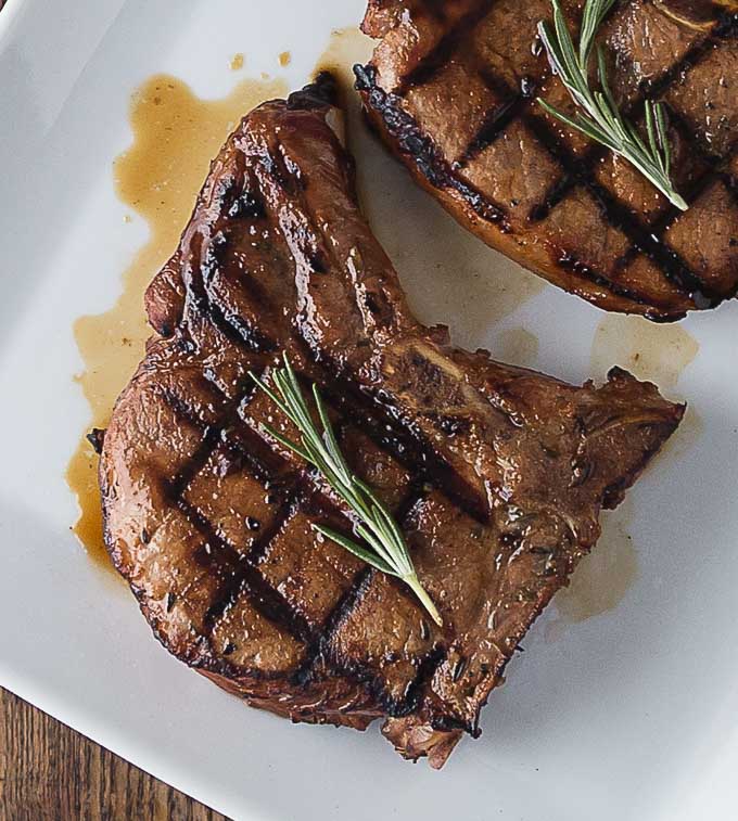 a closeup of grilled pork chops on a plate with sprigs of rosemary