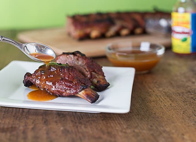 mango habanero ribs on a white plate with a spoon pouring sauce