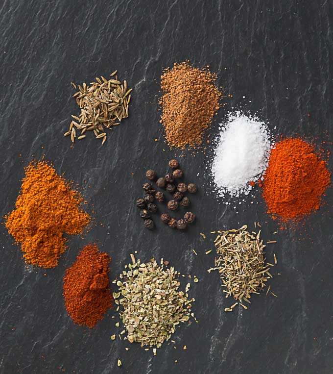 nine colorful piles of spices arranged in a circle on a black slate