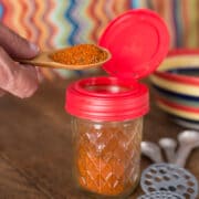A photo of homemade chili powder on a wooden spoon with a glass jar.