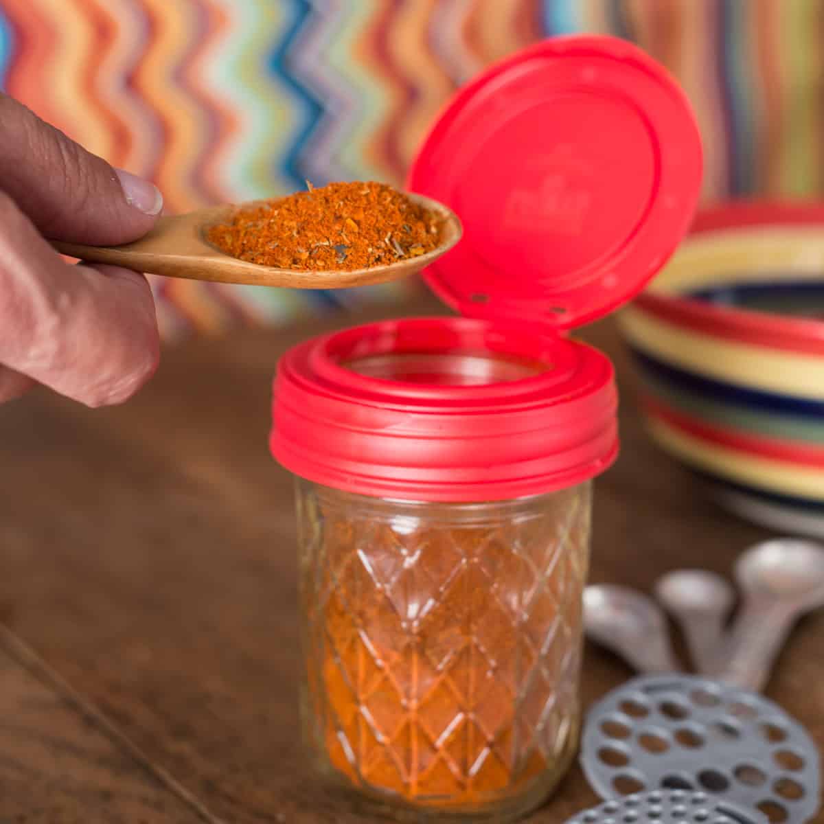 A photo of homemade chili powder on a wooden spoon with a glass jar.