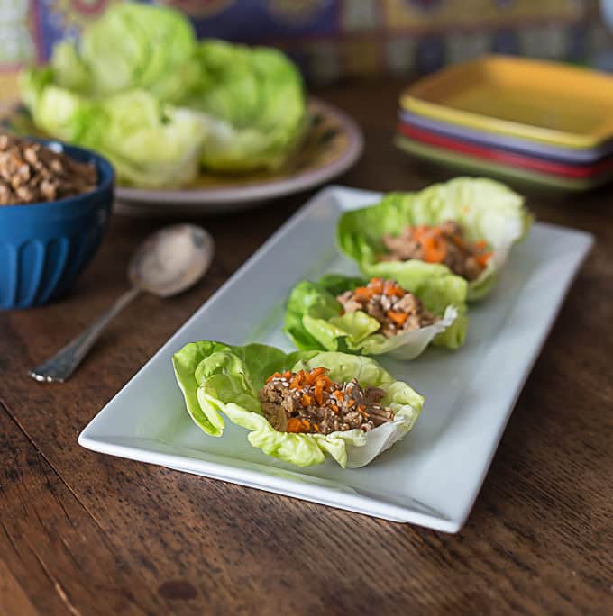 three lettuce wraps on a plate with a bowl of meat and lettuce on the left