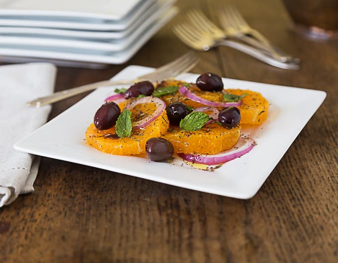 a white plate with turkish orange and onion salad with olives and mint leaves