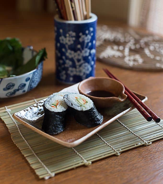 three pieces of sushi on a plate with soy sauce and chopsticks