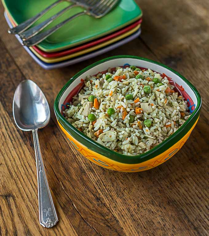 a bowl of rice with peas, carrots, and turkey with a spoon on the left