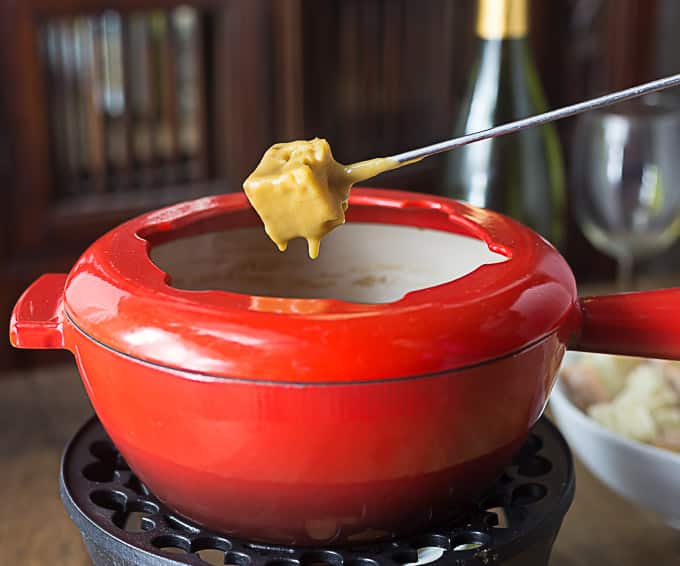a red fondue pot with a fondue fork dipped in bread and cheese