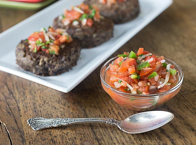 a white plate with black bean burgers and a bowl of tomato salsa on the right