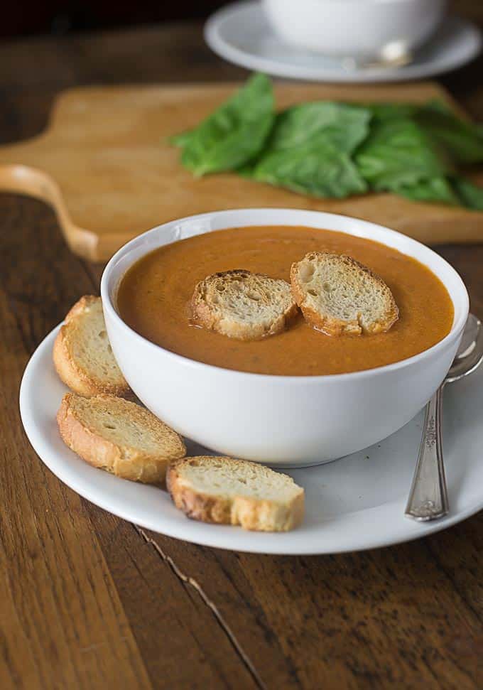 a bowl of tomato bisque with slices of baguette and sliced baguette on the side
