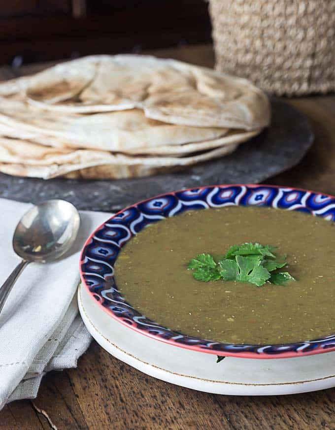 a bowl of middle eastern lentil sop with a spoon on the left and naan in the back