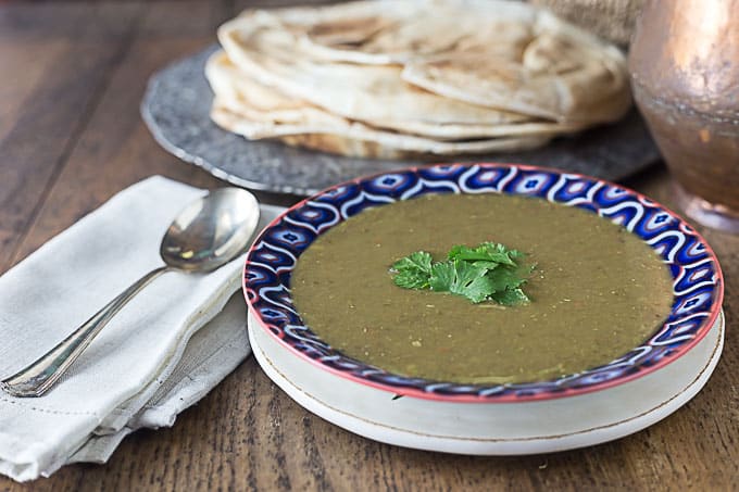 a bowl of middle eastern lentil soup with pieces of coriander and naan in the back