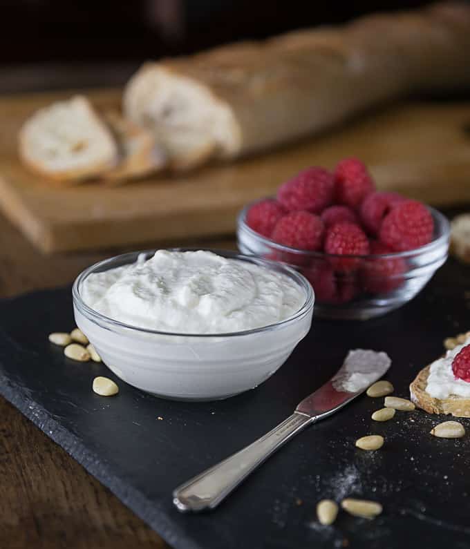 a close up of a bowl of ricotta and raspberries and a sliced baguette in the back