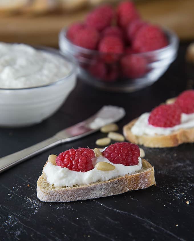 crostini with ricotta cheese and pine nuts with bowls of cheese and raspberries in the back