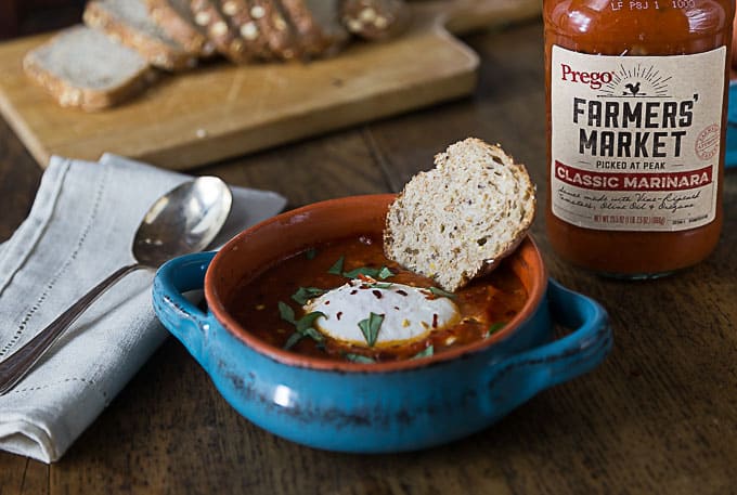 a poached egg in marinara sauce with a slice of bread a spoon on the left and a jar of sauce behind