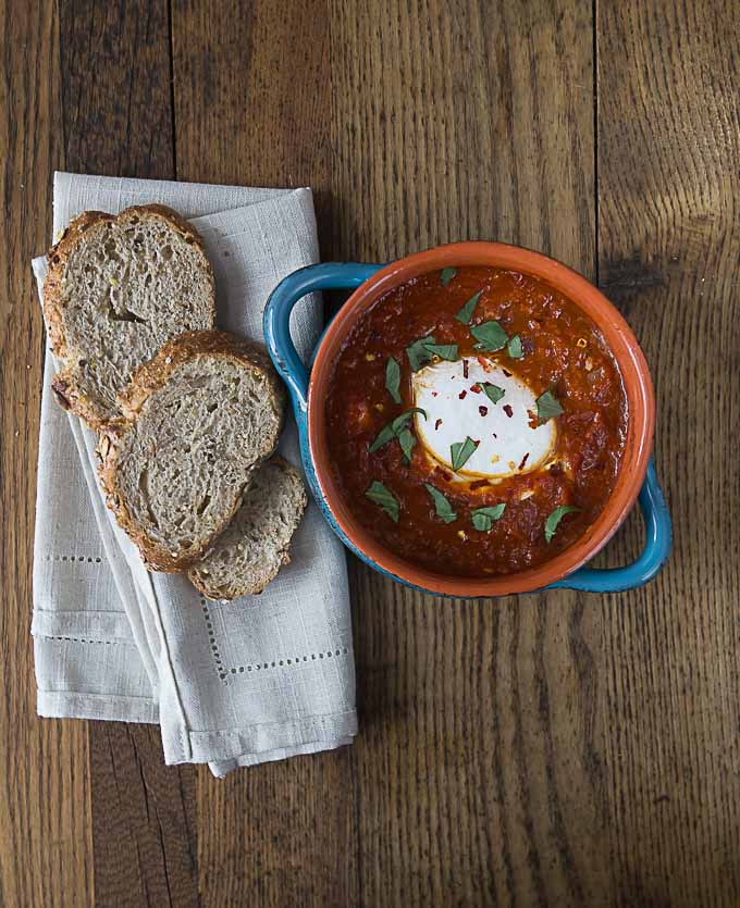 a poached egg in red sauce topped with basil and some bread on a napkin on the left