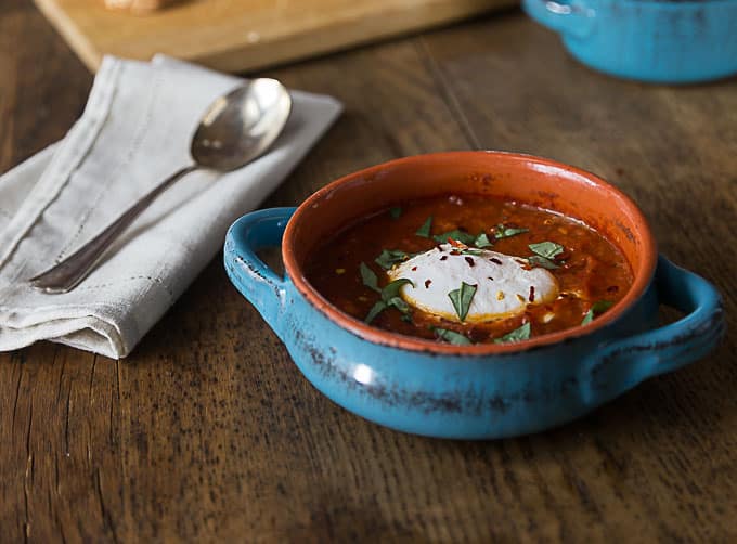 Spicy and saucy eggs in purgatory with fresh basil and a spoon on the left