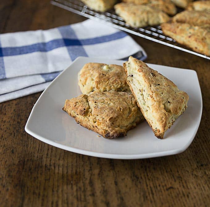 three scones on a plate with a napkin and scones on a drying rack in the back
