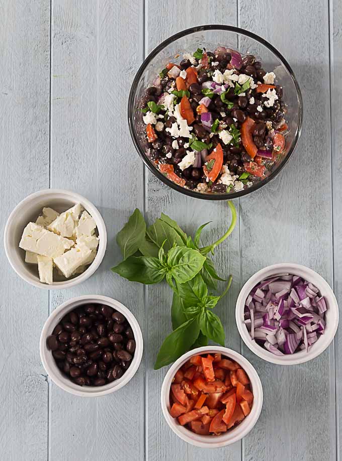 ingredients for blackbean tomato feta salad in separate bowls with a bowl of finished salad on top