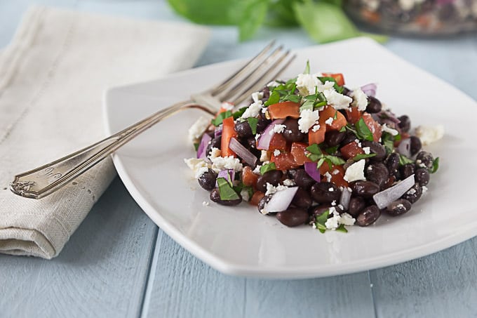 a white plate of blackbean, feta, and tomato salad with a fork and napkin on the left