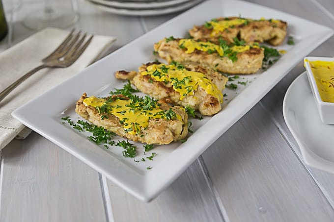 seared chicken breasts on a plate all topped with yellow creme sauce and parsley