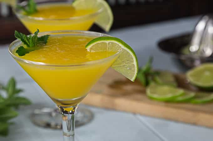 a closeup of a mango cocktail with a wedge of lime on the glass and mint 