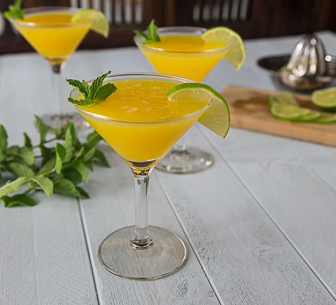 three martini glasses with mango cocktail and mint on the table. 