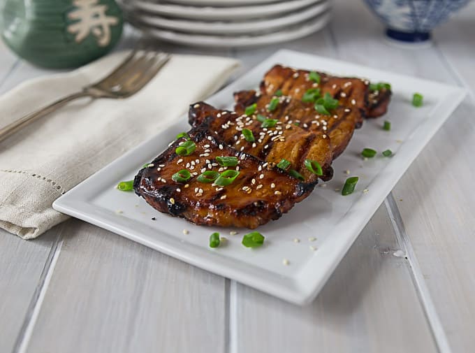 a plate of korean bbq grilled pork chops on a white plate with sesame seeds and green onions